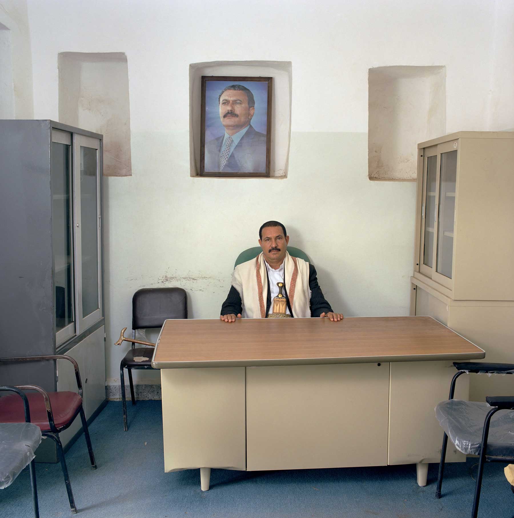 Yemen-16/2006 [Dhi., AA (b. 1955)]
Abdulwali Azablani (b. 1955) is head of the district of Dhi Sufal, Ibb Governorate. Monthly salary: 35,000 Rial ($ 196, euro 135).
Behind him a portrait of president Saleh of Yemen.