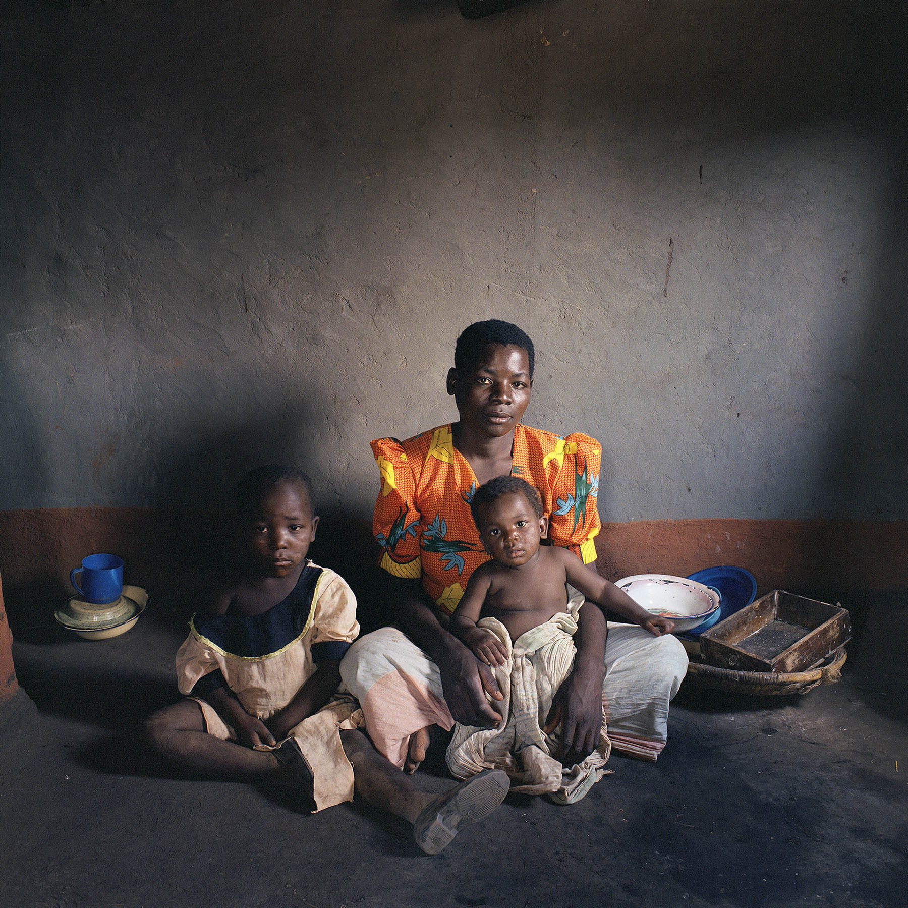 Malawi, Dickson, 11-2005.  She has contracted the aids virus. She is the only one in Dickson to admit it. Indoors only. To a stranger. Outside, nobody should know. In the village, only her parents are informed. They encourage her to persevere. Joyce Foliasi (27) with daughters Ndaziona (6) and Yankho (11 months). Ndaziona means: “I have a lot of worries”. Yankho is the local word for “answer”.  